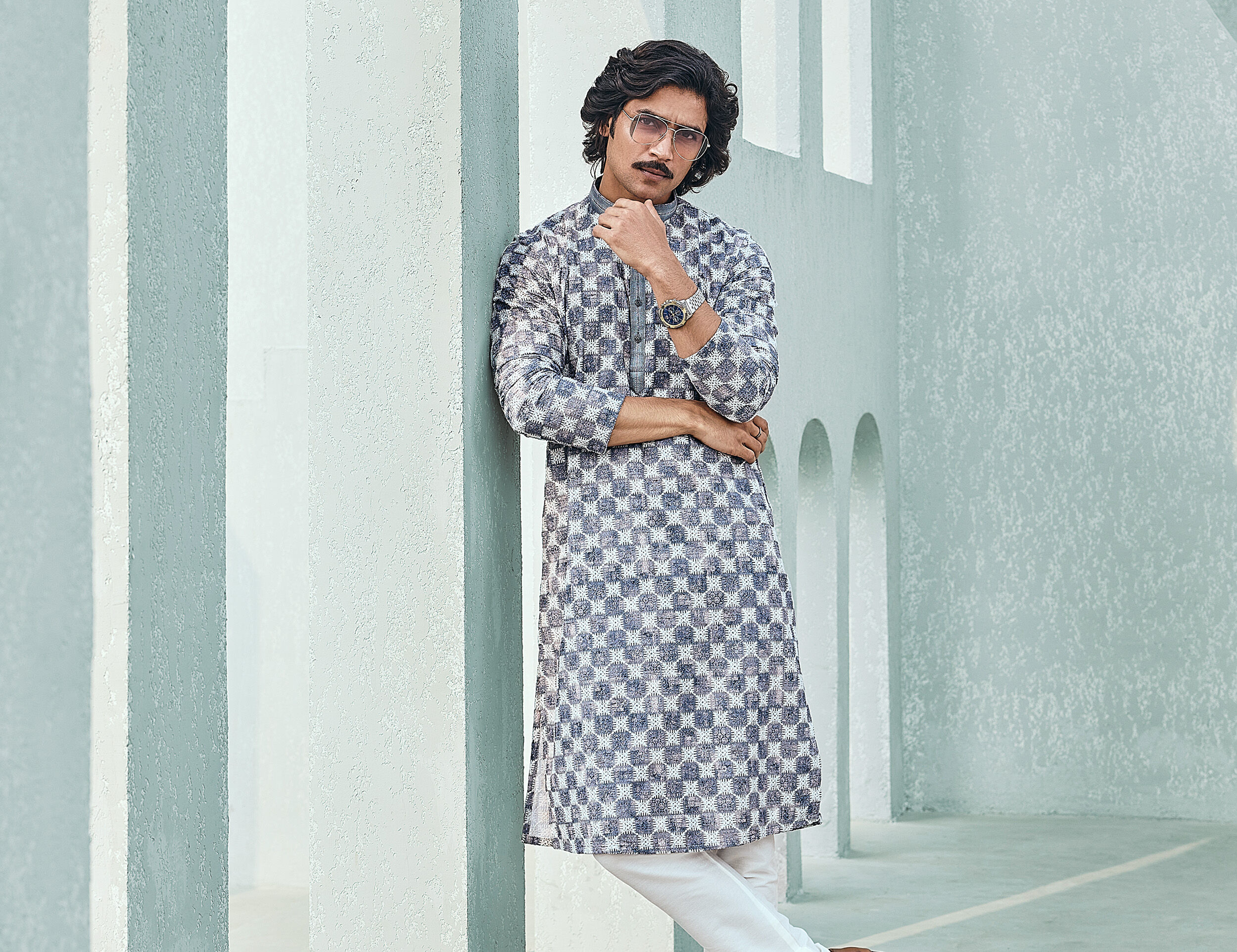 Stylish man wearing a modern printed kurta with white trousers, posing confidently against a minimalist architectural background